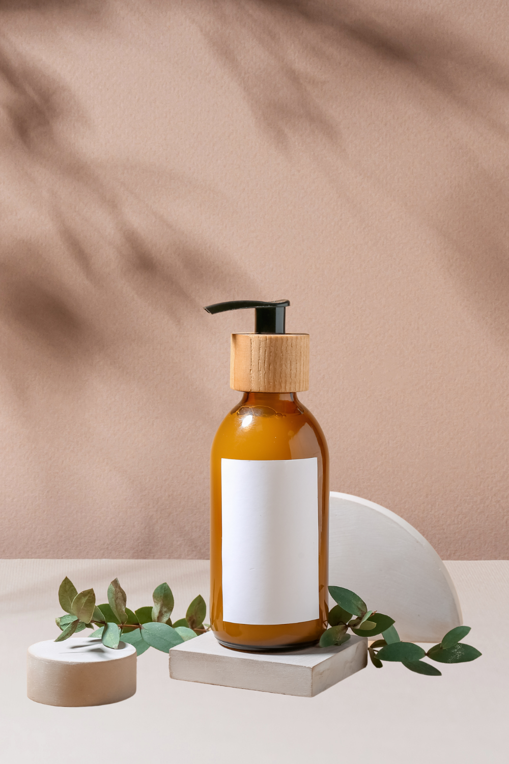 body wash glass bottle with leaves and nude artifacts on a nude background