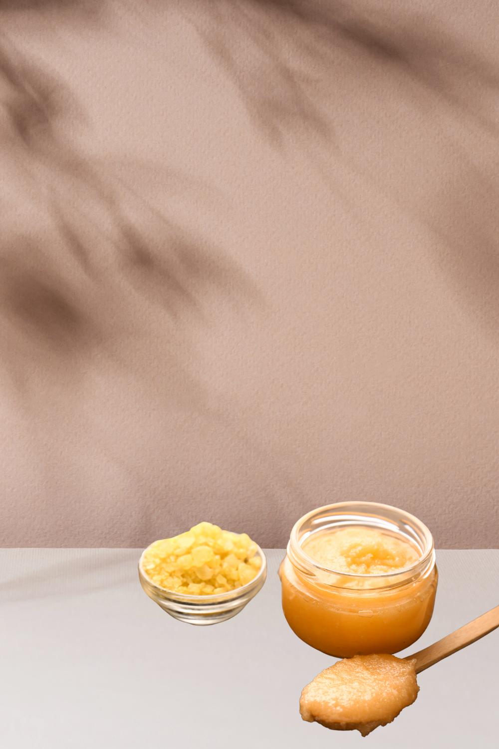 lip scrub, with a spoon full of scrub, and another sugary scrub in a bowl in front a nude wall