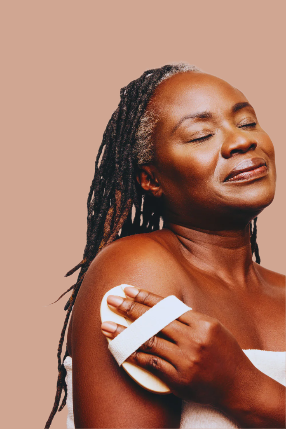 black woman brushes her skin with a dry brush with her eyes closed